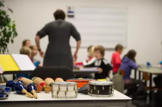 Nascholing muziek - Muziekinstrumenten met op de achtergrond een lerares die lesgeeft aan wat kinderen